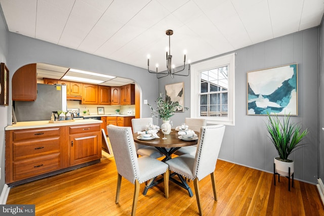 dining area featuring arched walkways, baseboard heating, an inviting chandelier, and light wood-style floors