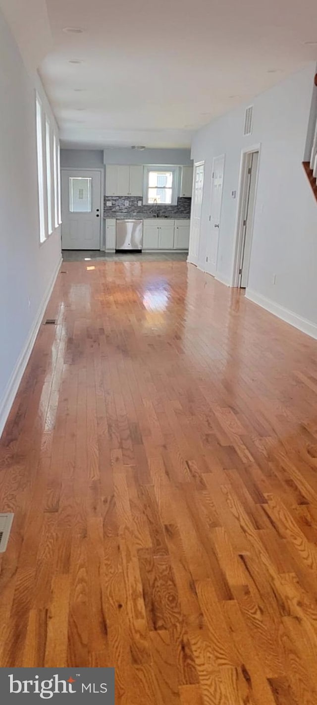 unfurnished living room with a sink, light wood-style flooring, visible vents, and baseboards