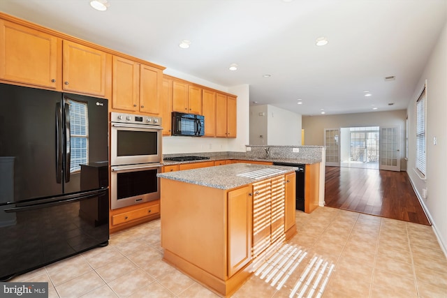 kitchen with sink, light stone counters, a center island, light tile patterned floors, and black appliances