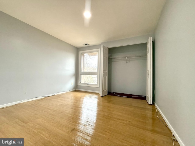 unfurnished bedroom with a closet, wood finished floors, visible vents, and baseboards