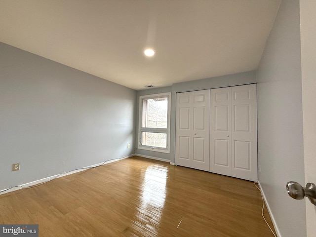 unfurnished bedroom featuring a closet, wood finished floors, visible vents, and baseboards