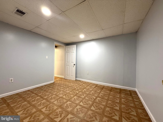 basement with a paneled ceiling, visible vents, and baseboards