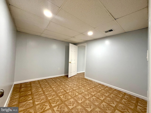 basement featuring visible vents, a drop ceiling, and baseboards