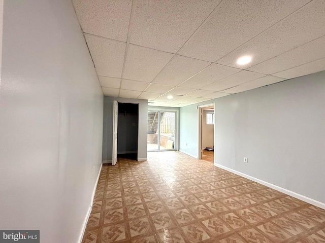 interior space featuring a paneled ceiling, light floors, and baseboards