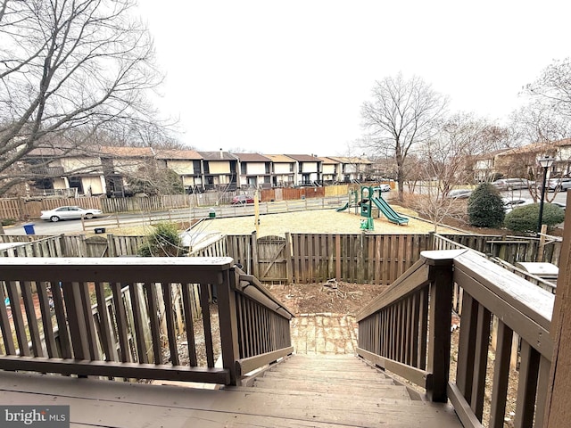 wooden deck featuring a residential view, fence, and playground community