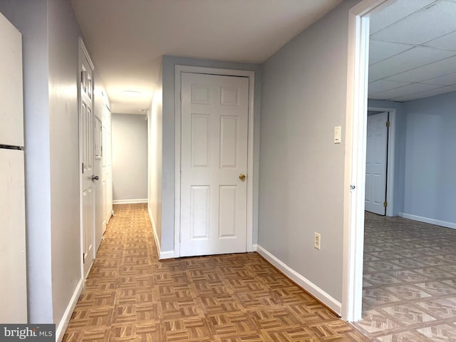 hallway featuring a paneled ceiling and baseboards