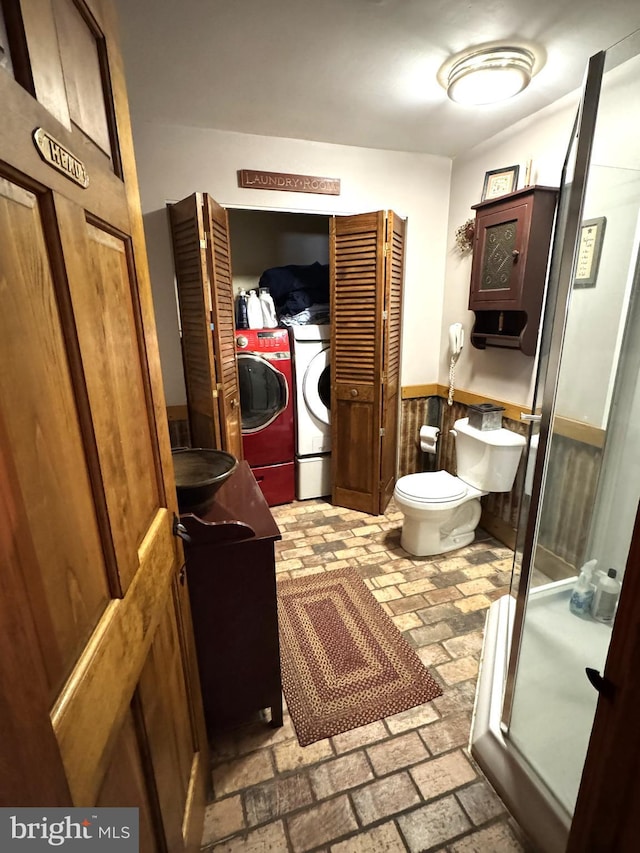 bathroom with vanity, toilet, separate washer and dryer, and a shower with door