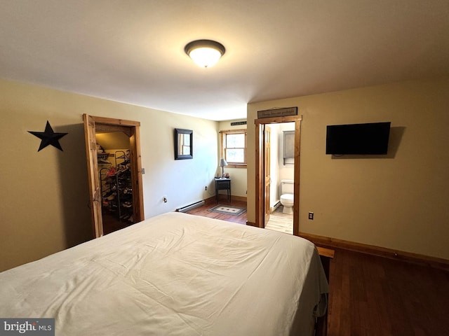 bedroom with hardwood / wood-style flooring, a baseboard heating unit, and connected bathroom