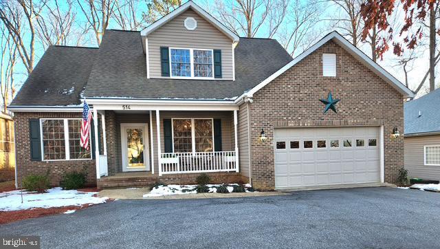 view of front of house with driveway, roof with shingles, an attached garage, covered porch, and brick siding