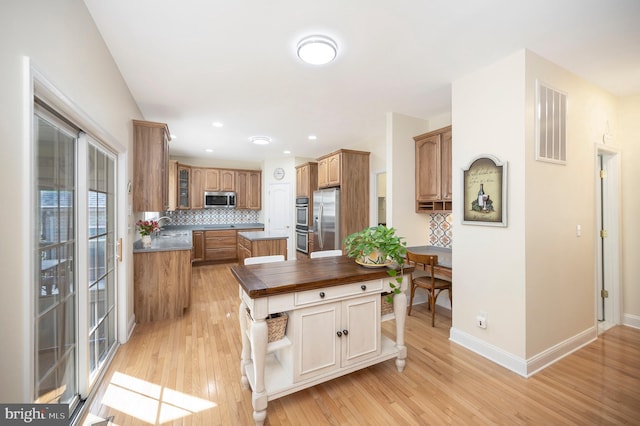 kitchen featuring visible vents, light wood-style floors, appliances with stainless steel finishes, backsplash, and glass insert cabinets