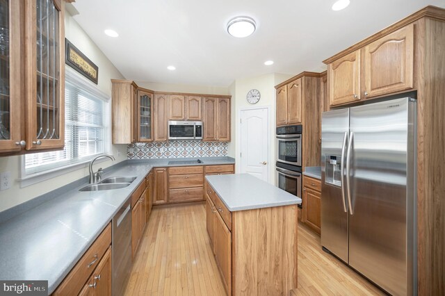 kitchen with stainless steel appliances, light wood-style flooring, decorative backsplash, a sink, and a kitchen island