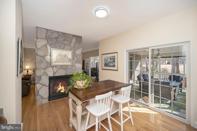 dining space with crown molding, a stone fireplace, and hardwood / wood-style flooring