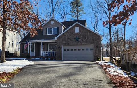 traditional home featuring driveway, covered porch, a garage, and brick siding