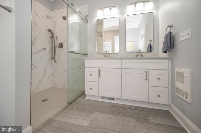 bathroom with double vanity, a marble finish shower, visible vents, heating unit, and a sink