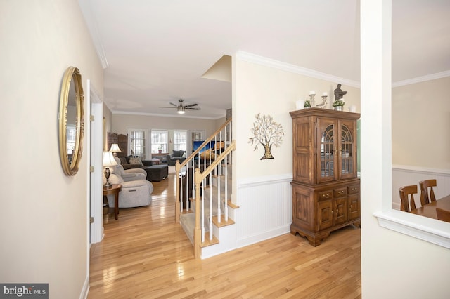 hallway with light wood-type flooring, a wainscoted wall, stairs, and ornamental molding