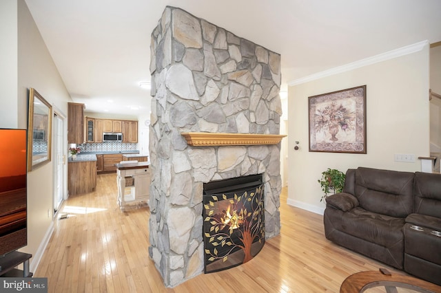 living area featuring light wood-style flooring, baseboards, crown molding, and a stone fireplace