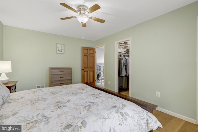 bedroom with baseboards, visible vents, wood finished floors, a walk in closet, and a closet