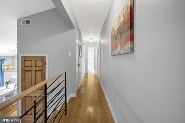 hallway with baseboards, visible vents, an upstairs landing, light wood-type flooring, and a notable chandelier