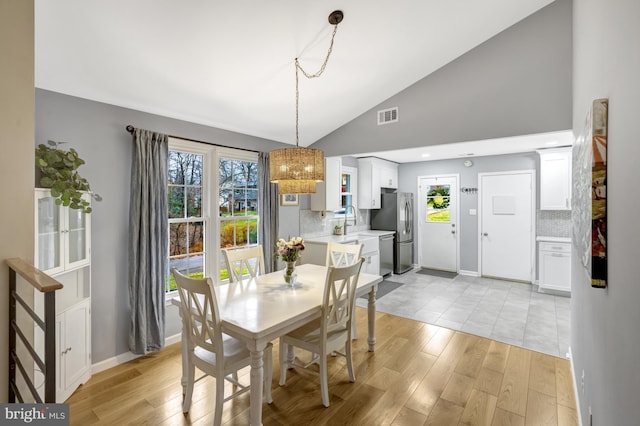 dining room with light wood-type flooring, high vaulted ceiling, baseboards, and visible vents