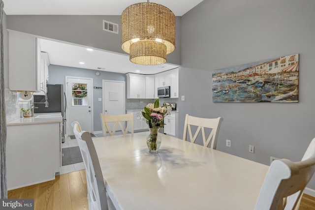 dining space featuring light wood-type flooring, visible vents, vaulted ceiling, and a notable chandelier