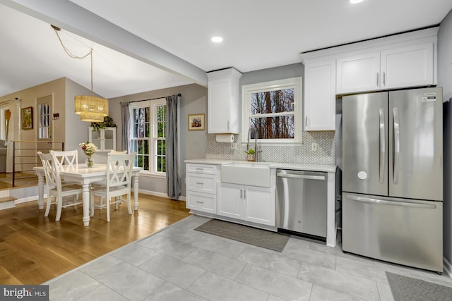 kitchen with tasteful backsplash, white cabinets, stainless steel appliances, light countertops, and a sink