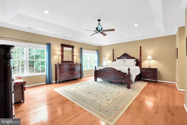 bedroom featuring a raised ceiling, ceiling fan, and light wood-type flooring