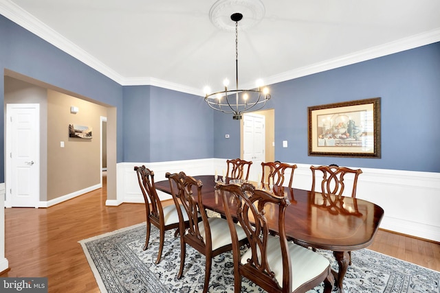 dining space with wood-type flooring, an inviting chandelier, and crown molding