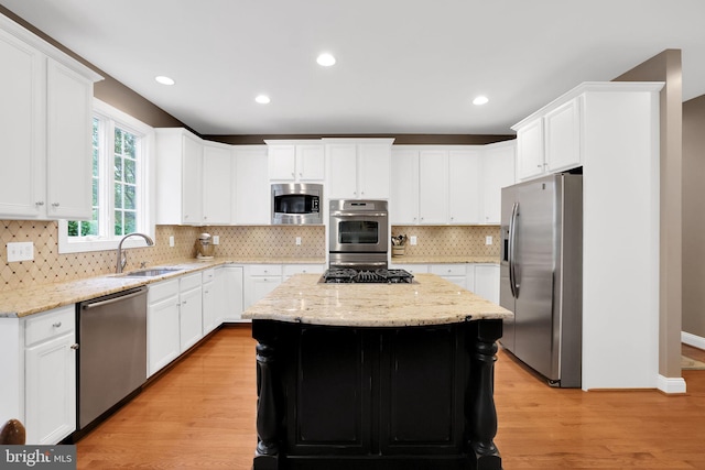 kitchen featuring sink, light hardwood / wood-style flooring, appliances with stainless steel finishes, a kitchen island, and light stone countertops