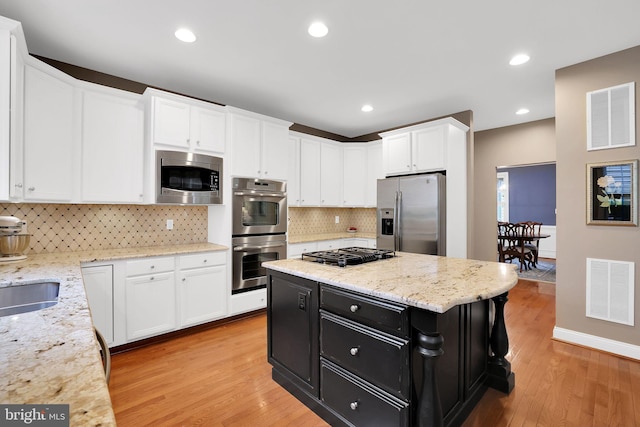 kitchen featuring stainless steel appliances, a center island, light stone counters, white cabinets, and light wood-type flooring