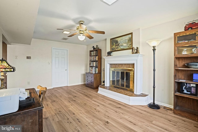 living room featuring a fireplace, ceiling fan, and light hardwood / wood-style floors