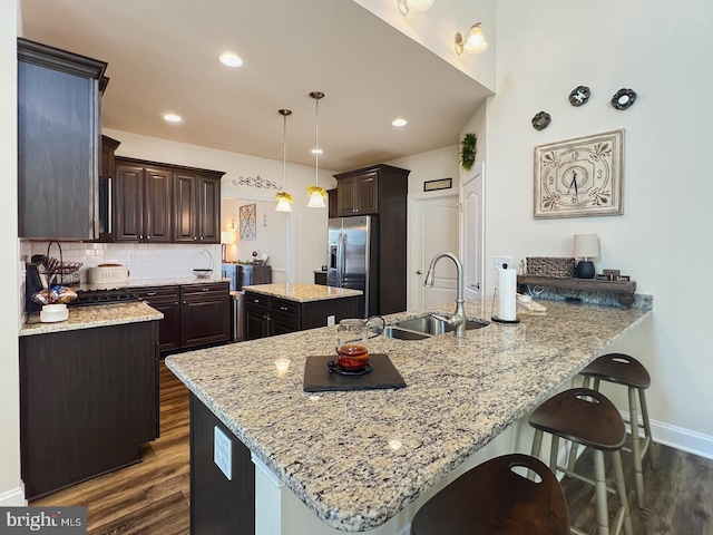 kitchen featuring pendant lighting, sink, a center island, light stone counters, and stainless steel fridge with ice dispenser