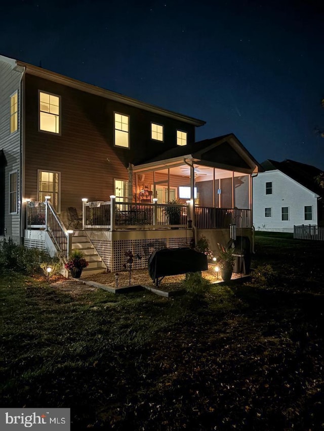 back house at twilight with a sunroom and a lawn