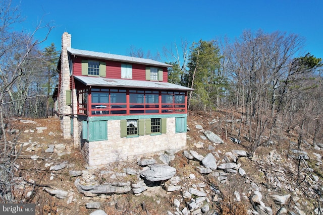 exterior space with metal roof, stone siding, and a chimney