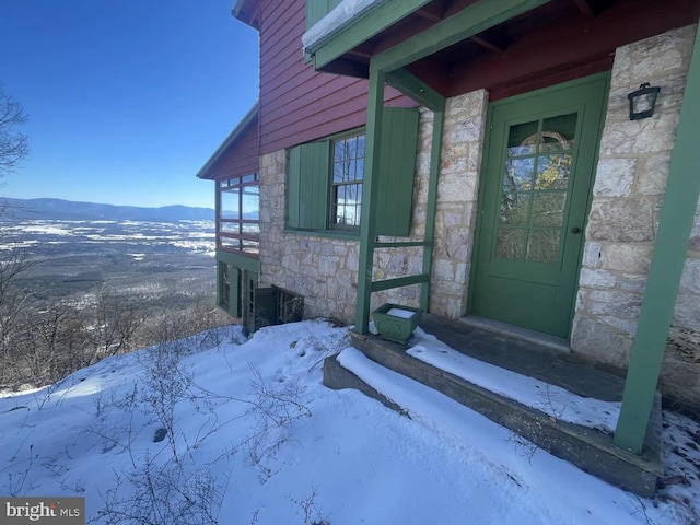 snow covered property entrance featuring stone siding and a mountain view