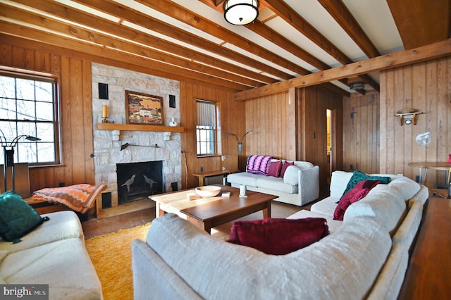 living area featuring beamed ceiling, a healthy amount of sunlight, a stone fireplace, and wooden walls