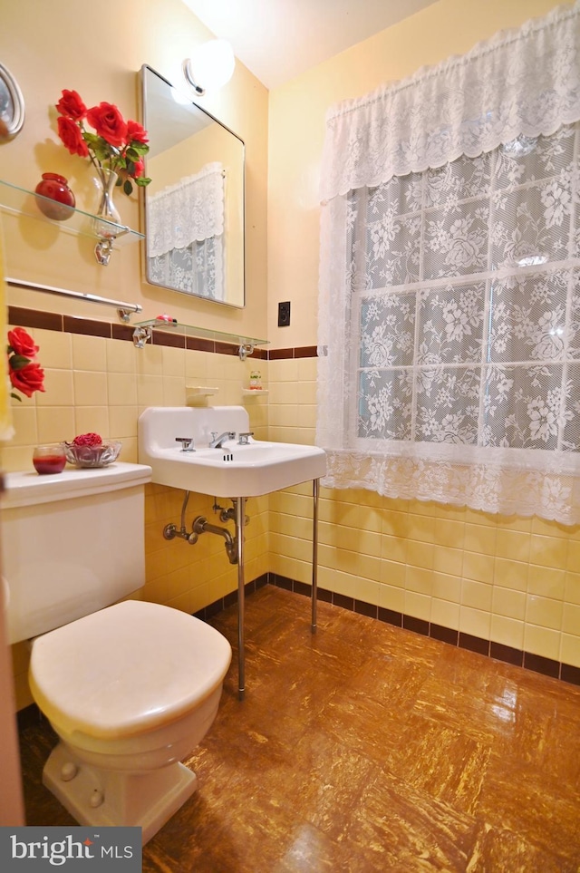 bathroom with tile walls, toilet, a wainscoted wall, and a sink