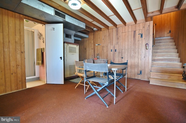 dining space with beamed ceiling, wooden walls, and stairway