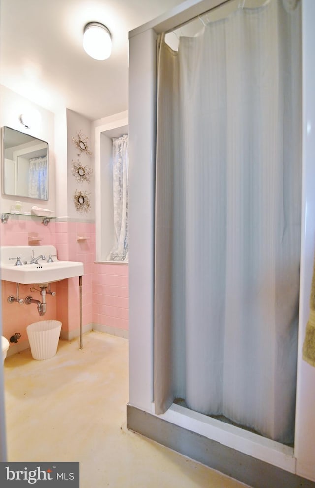 bathroom featuring tile walls, a shower with curtain, wainscoting, and a sink