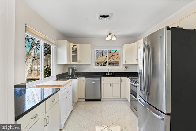 kitchen with light tile patterned flooring, stainless steel appliances, a sink, visible vents, and tasteful backsplash