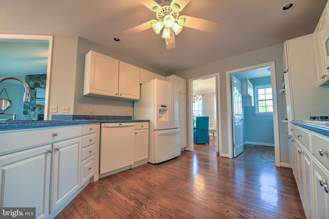 kitchen featuring white appliances, a sink, white cabinets, dark countertops, and dark wood finished floors