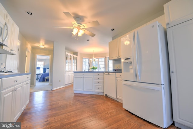 kitchen featuring a wealth of natural light, white cabinetry, wood finished floors, white appliances, and a peninsula