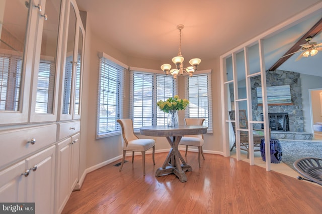 dining space with light wood-style flooring, baseboards, a stone fireplace, and lofted ceiling with beams