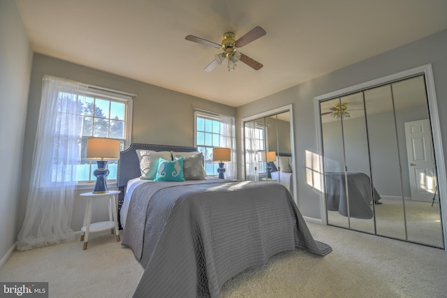 carpeted bedroom featuring multiple closets, multiple windows, baseboards, and a ceiling fan