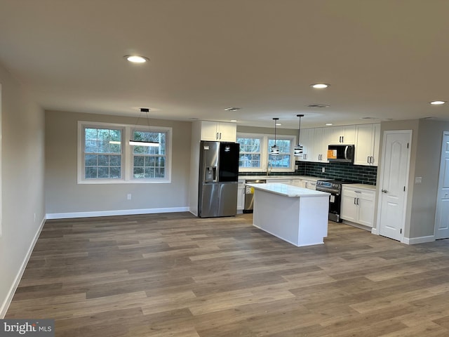 kitchen featuring white cabinetry, hanging light fixtures, stainless steel appliances, a center island, and backsplash