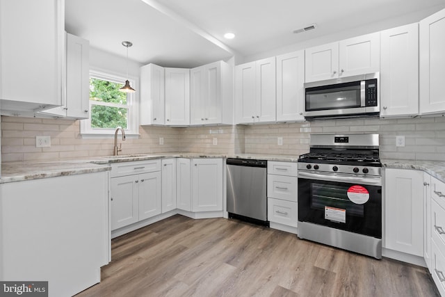 kitchen with pendant lighting, appliances with stainless steel finishes, sink, and white cabinets