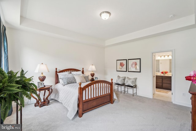 bedroom with ensuite bathroom, light colored carpet, and a tray ceiling