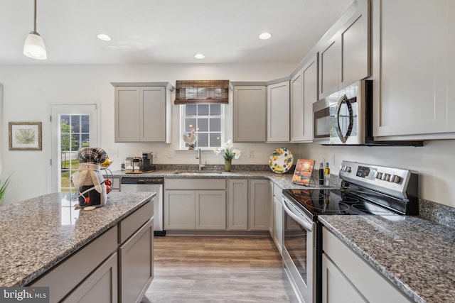 kitchen with sink, stone counters, appliances with stainless steel finishes, decorative light fixtures, and light wood-type flooring