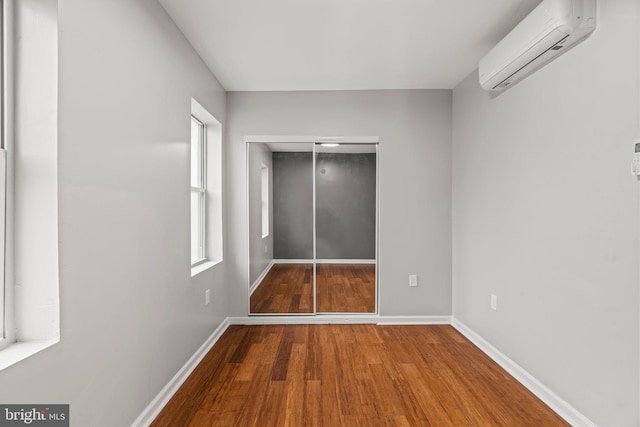 unfurnished bedroom featuring hardwood / wood-style flooring, a wall mounted AC, and a closet