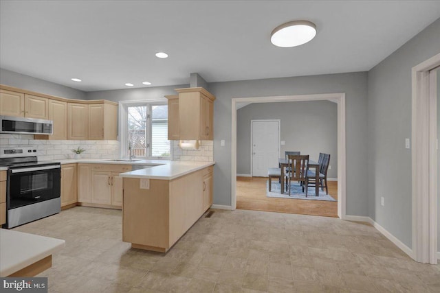 kitchen with light brown cabinets, a peninsula, light countertops, appliances with stainless steel finishes, and tasteful backsplash