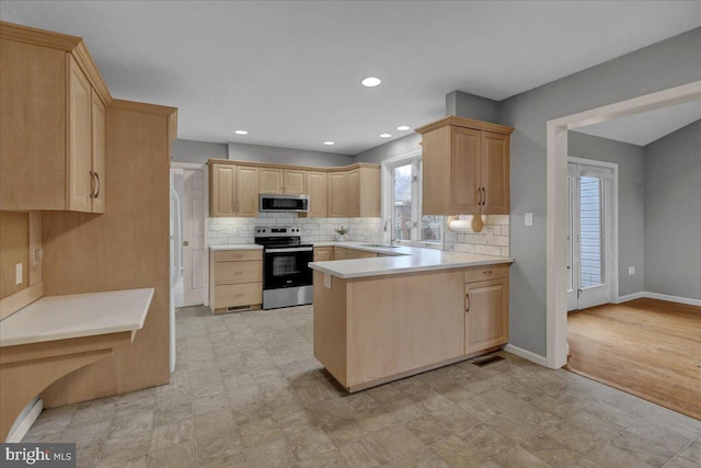 kitchen featuring stainless steel appliances, light countertops, backsplash, light brown cabinets, and a sink